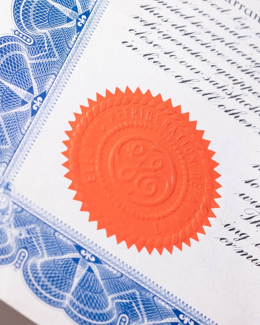 Close-up of a historical patent document with embossed red seal, blue engraved border, and copperplate script